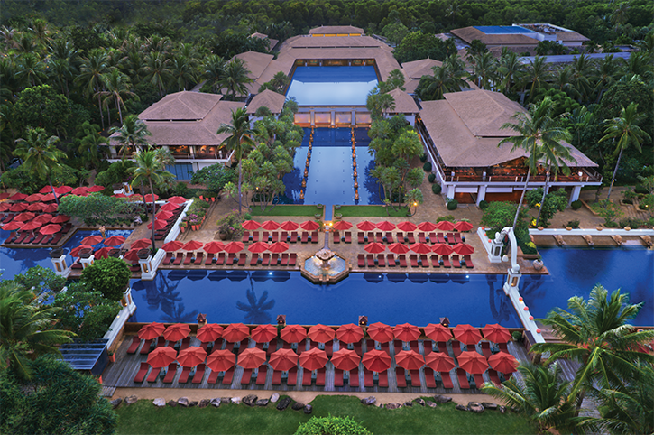 Aerial view of beautiful tropical resort with shimmering pools and many red deck chairs and umbrellas
