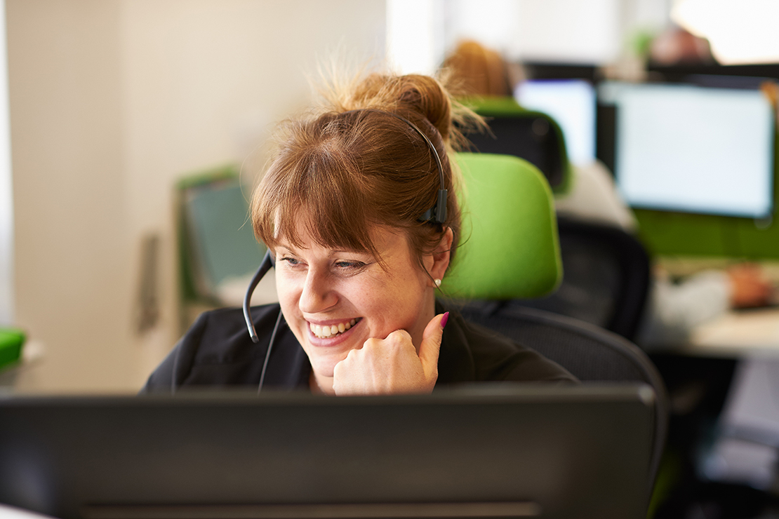 Smiling owner and member services associate in a call center wearing a headset, white shirt and navy blue jacket
